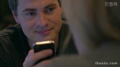 特写镜头，<strong>一个</strong>高兴的年轻人在智能手机上输入短信，而他的朋友正在和他说话